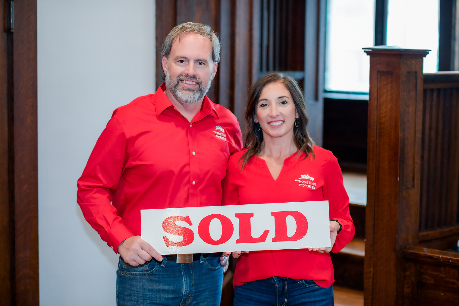 Samantha Carver and Rob Ranard holding a SOLD sign in a warm interior, behind a legibility scrim.